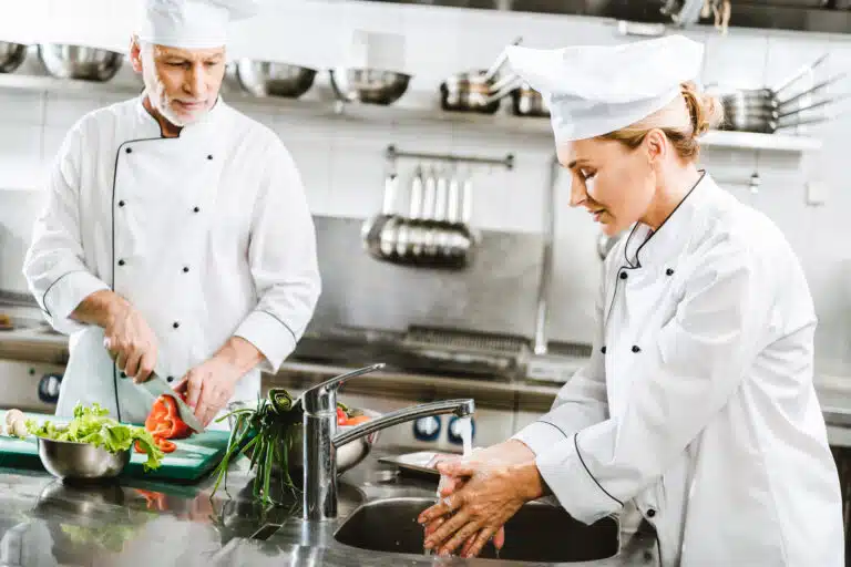 selective focus of male and female chefs in double-breasted jackets cooking in restaurant kitchen