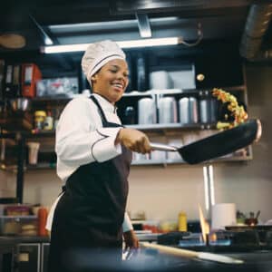 African American female chef having fun while preparing food in the kitchen at restaurant.