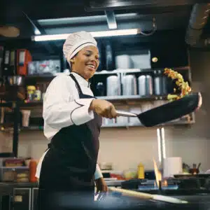 African American female chef having fun while preparing food in the kitchen at restaurant.
