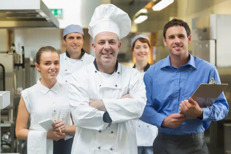 Head chef posing with the team behind him in a profesional kitchen
