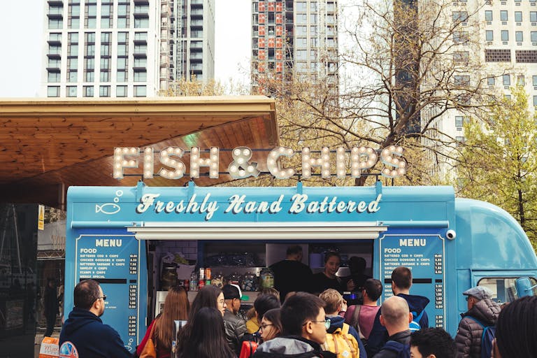 Crowd enjoying fish and chips at a lively food truck with urban buildings in the background.