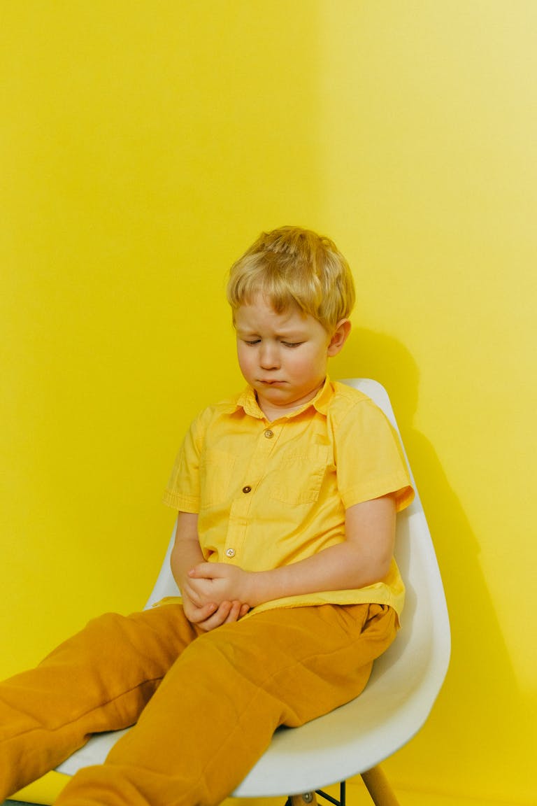 A young boy in yellow clothing displays sadness while sitting against a bright yellow background.